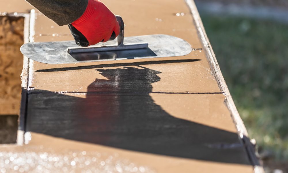 Construction Worker Using Trowel On Wet Cement Forming Coping Around New Pool.