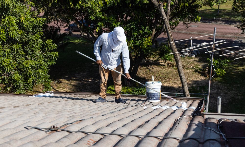 Worker adding undercoat foundation paint onto rooftop with roller as primer at residential building in renovation